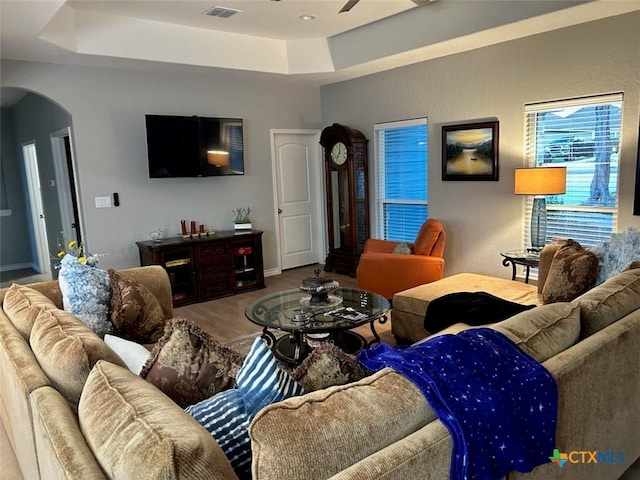 living room featuring arched walkways, a tray ceiling, a ceiling fan, and wood finished floors