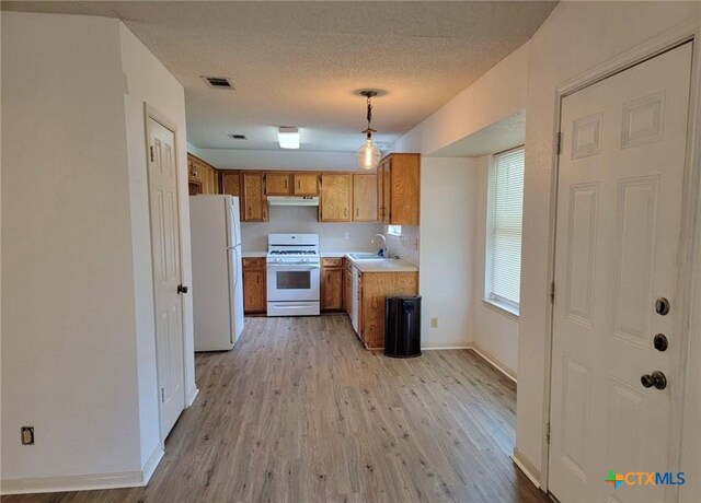 kitchen with a textured ceiling, sink, pendant lighting, light wood-type flooring, and white appliances