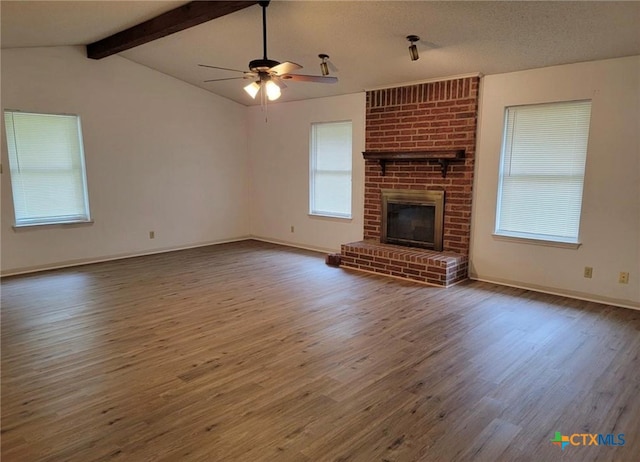 unfurnished living room featuring ceiling fan, a textured ceiling, hardwood / wood-style floors, a brick fireplace, and lofted ceiling with beams