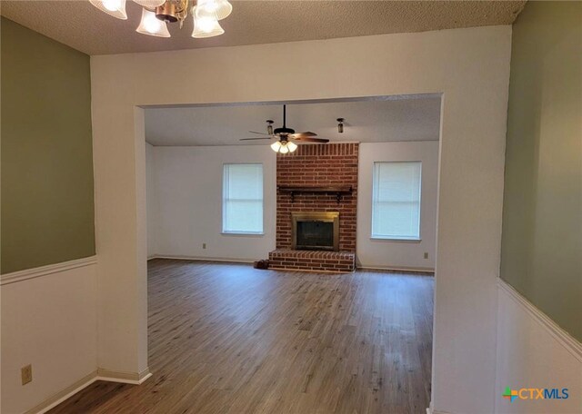 unfurnished living room with hardwood / wood-style floors, a textured ceiling, ceiling fan with notable chandelier, and a fireplace