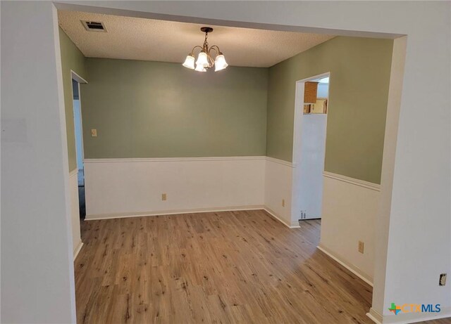 empty room with light wood-type flooring, a textured ceiling, and an inviting chandelier