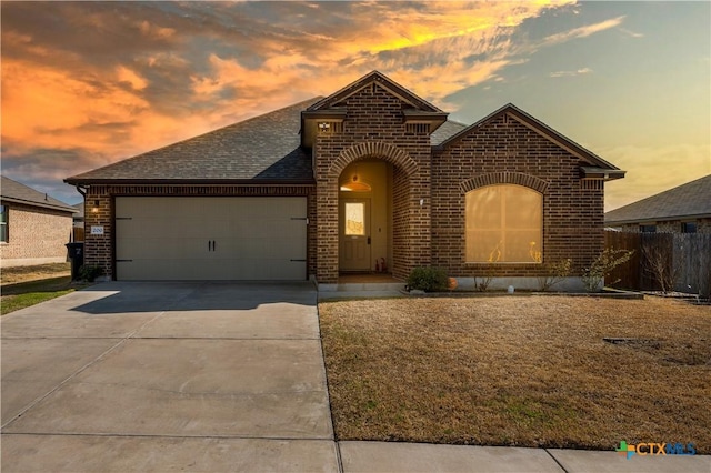 view of front of property featuring a garage, driveway, brick siding, and roof with shingles