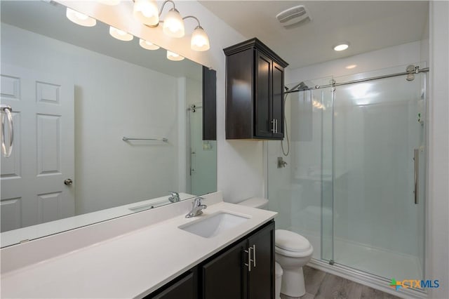 bathroom featuring toilet, wood finished floors, vanity, visible vents, and a stall shower