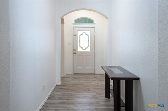 foyer entrance featuring arched walkways, wood finished floors, and baseboards