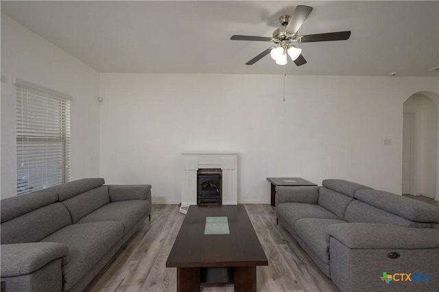 living area featuring arched walkways, a ceiling fan, baseboards, light wood-type flooring, and a wood stove