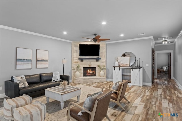 living room featuring ceiling fan, a stone fireplace, crown molding, and light hardwood / wood-style floors