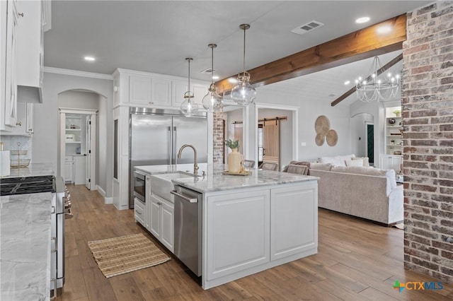 kitchen featuring light stone counters, decorative light fixtures, stainless steel appliances, a barn door, and white cabinets