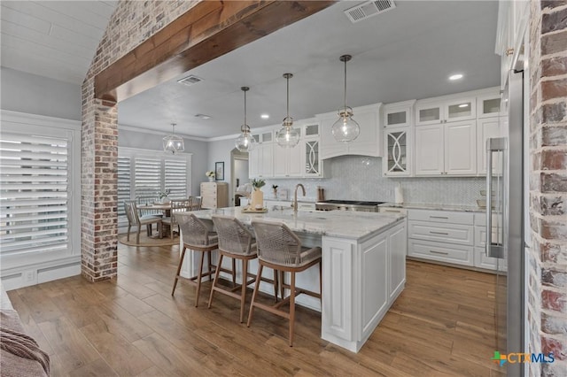 kitchen featuring decorative light fixtures, light stone countertops, an island with sink, and white cabinets