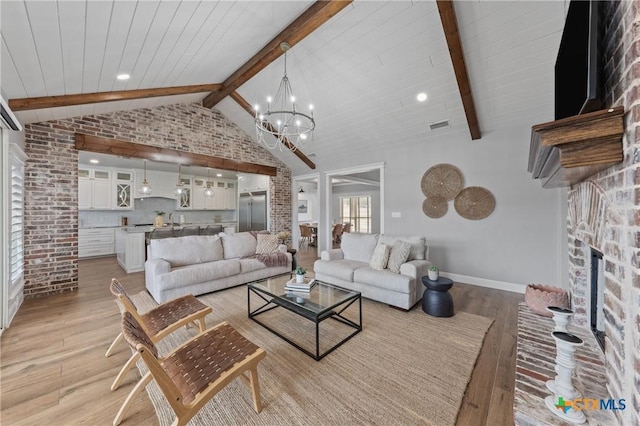 living room with light hardwood / wood-style flooring, high vaulted ceiling, a chandelier, brick wall, and beamed ceiling