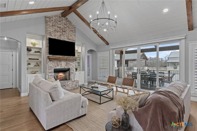 living room featuring beamed ceiling, a brick fireplace, an inviting chandelier, and light hardwood / wood-style flooring