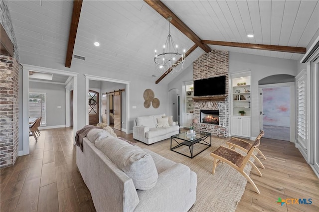 living room featuring a notable chandelier, lofted ceiling with beams, light hardwood / wood-style floors, a brick fireplace, and built in shelves