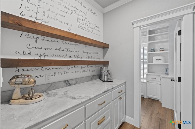 bar with light stone counters, ornamental molding, light hardwood / wood-style floors, and white cabinets