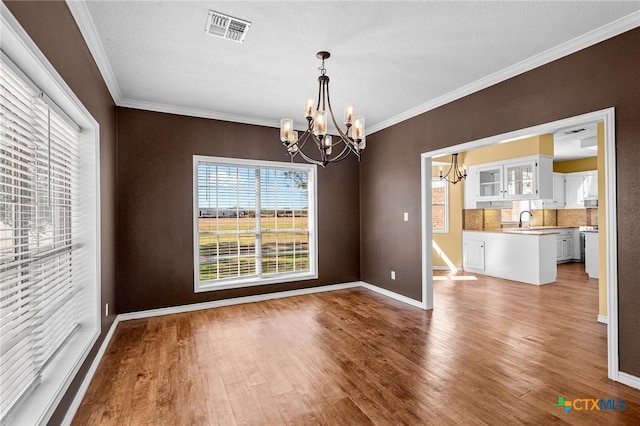 unfurnished dining area featuring crown molding, sink, hardwood / wood-style floors, and a notable chandelier