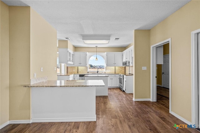 kitchen with appliances with stainless steel finishes, white cabinetry, light stone counters, dark hardwood / wood-style flooring, and kitchen peninsula