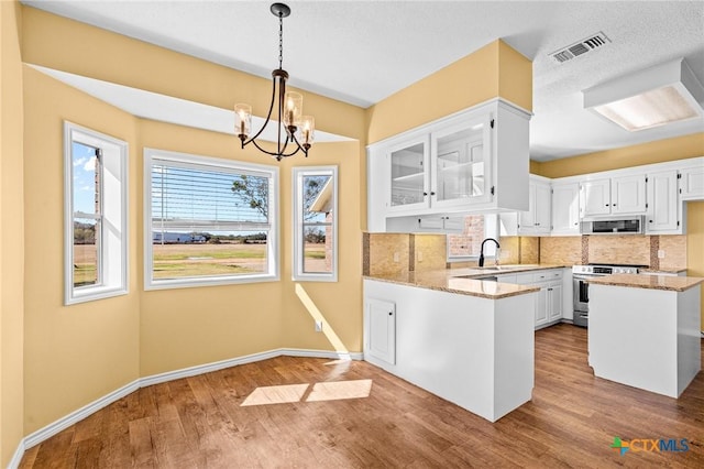 kitchen featuring stainless steel electric range, kitchen peninsula, white cabinets, light stone countertops, and backsplash