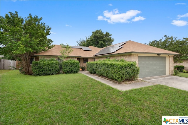 ranch-style home with a garage, solar panels, and a front yard