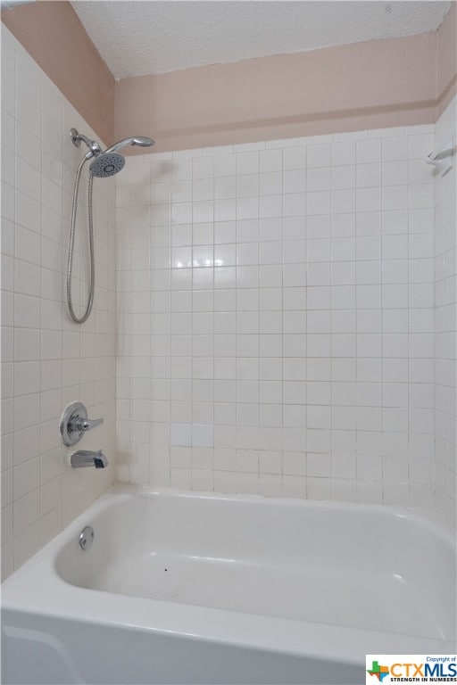 bathroom with a textured ceiling and tiled shower / bath