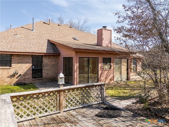 rear view of property with brick siding, a chimney, a wooden deck, and roof with shingles