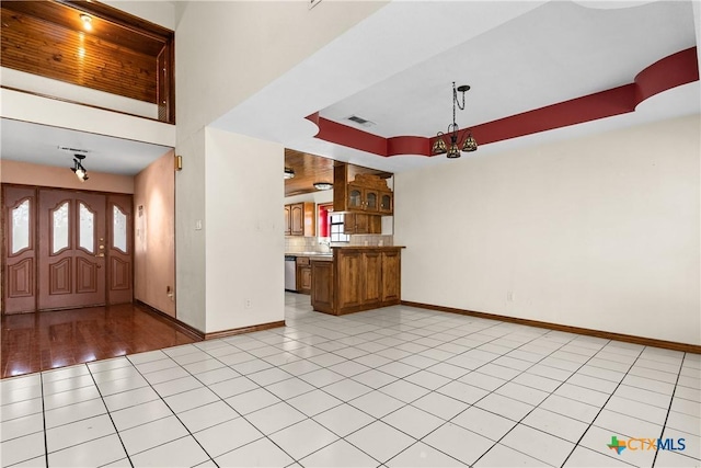 entryway featuring light tile patterned floors, visible vents, baseboards, a tray ceiling, and a chandelier