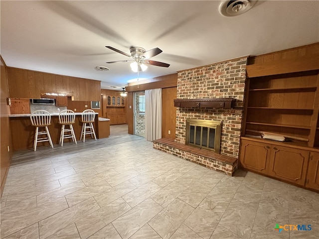 2602 Miori Ln, Victoria, TX 77901 - unfurnished living room featuring wood walls, a ceiling fan, and a fireplace