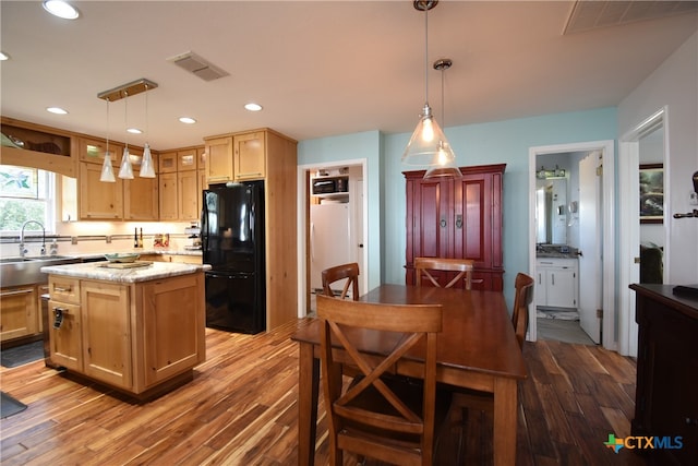 kitchen with hanging light fixtures, hardwood / wood-style flooring, black fridge, and a kitchen island