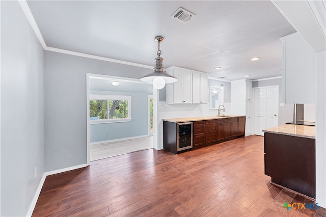 kitchen with wood-type flooring, white cabinetry, dark brown cabinets, light stone countertops, and beverage cooler