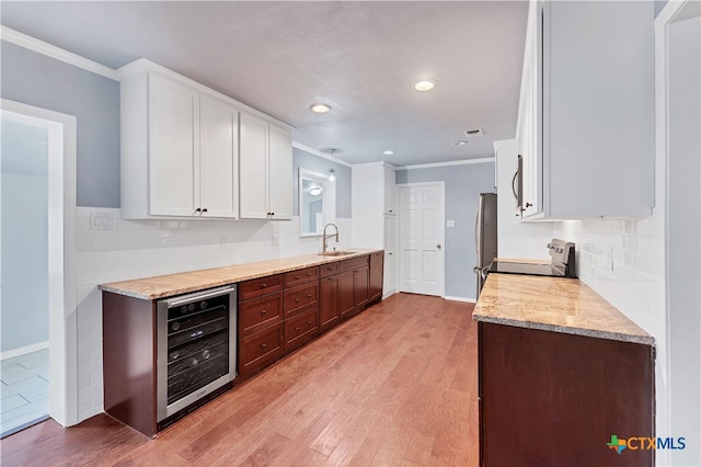 kitchen with stainless steel appliances, beverage cooler, sink, white cabinetry, and light hardwood / wood-style flooring