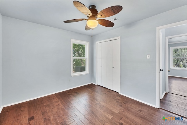 unfurnished bedroom with dark hardwood / wood-style flooring, multiple windows, ceiling fan, and a closet