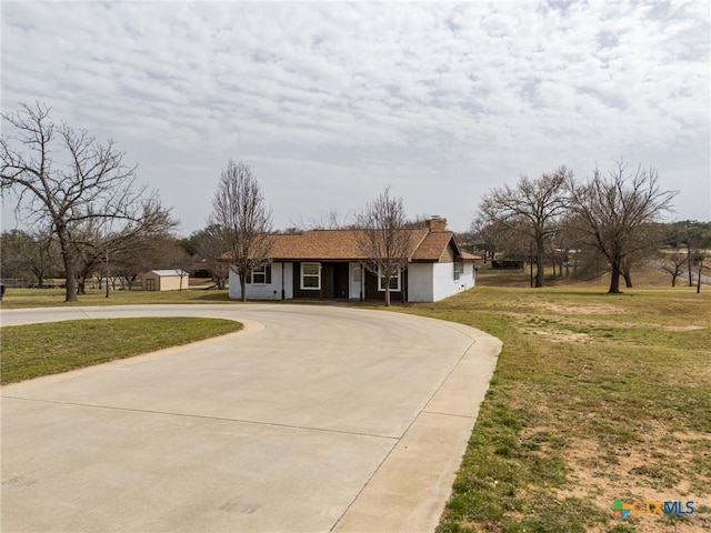 view of front of house featuring curved driveway, a chimney, and a front lawn