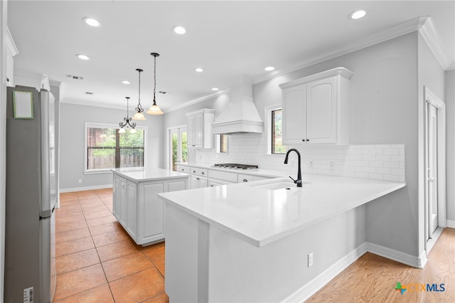 kitchen featuring kitchen peninsula, custom range hood, sink, white cabinets, and a kitchen island