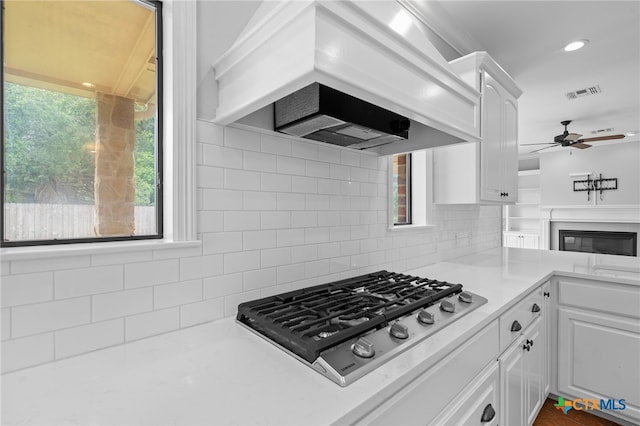 kitchen with ceiling fan, gas cooktop, tasteful backsplash, white cabinets, and custom range hood