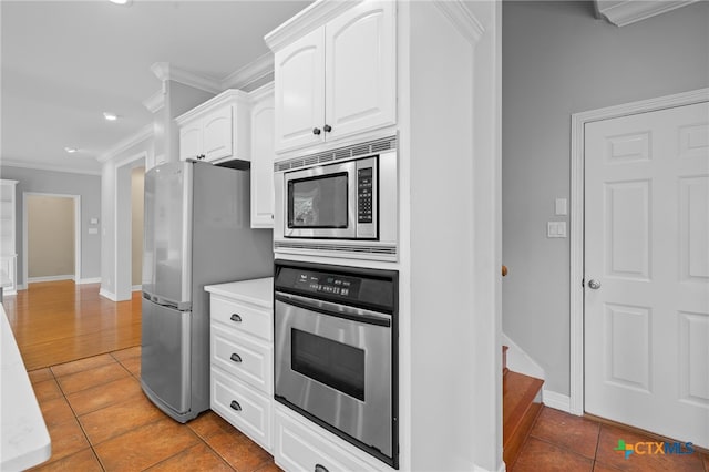 kitchen with dark tile patterned floors, white cabinets, stainless steel appliances, and ornamental molding