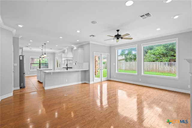 unfurnished living room featuring ceiling fan, sink, light wood-type flooring, and crown molding