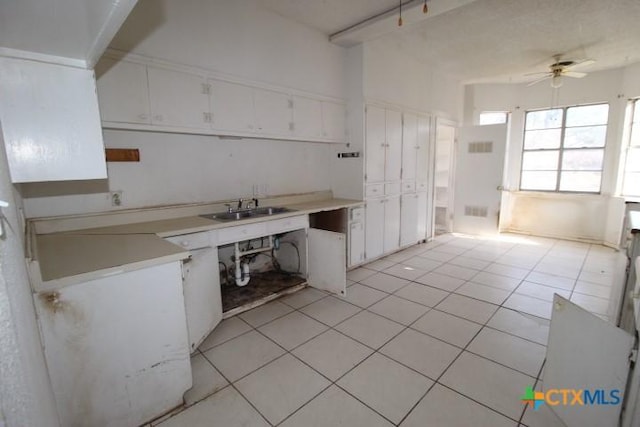 kitchen with light tile patterned flooring, a sink, a ceiling fan, white cabinets, and light countertops