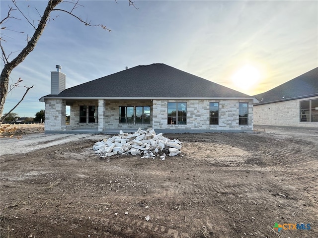 rear view of property featuring stone siding and a chimney