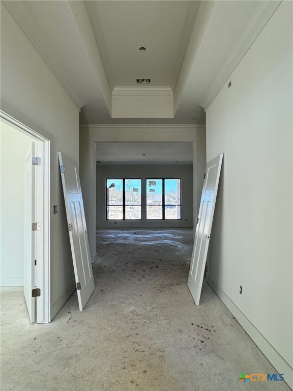 hall with baseboards, a raised ceiling, and crown molding