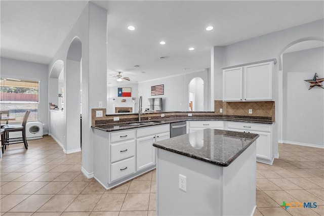 kitchen with a ceiling fan, a sink, dark stone countertops, tasteful backsplash, and light tile patterned floors