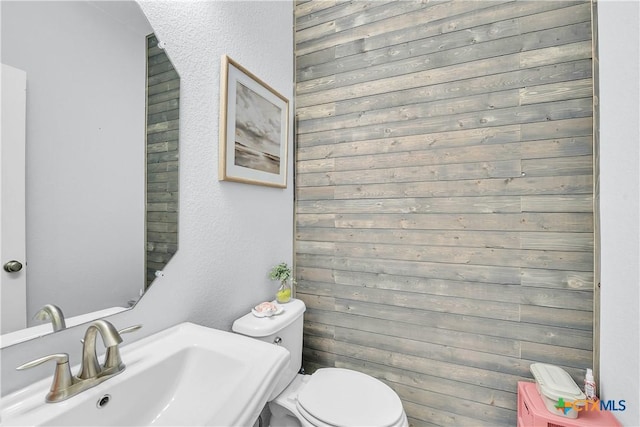 half bath featuring toilet, a textured wall, and a sink