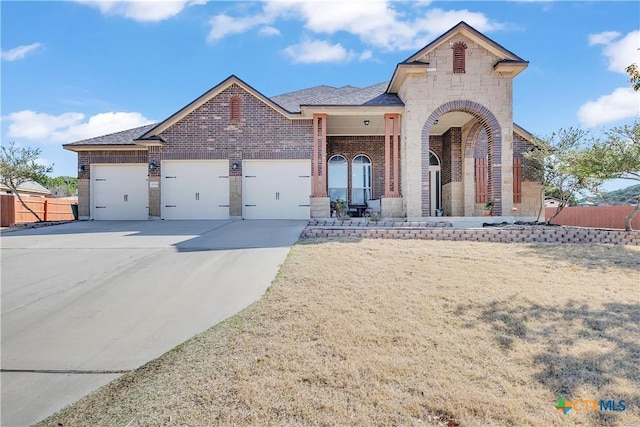 french provincial home featuring brick siding, fence, concrete driveway, a garage, and stone siding