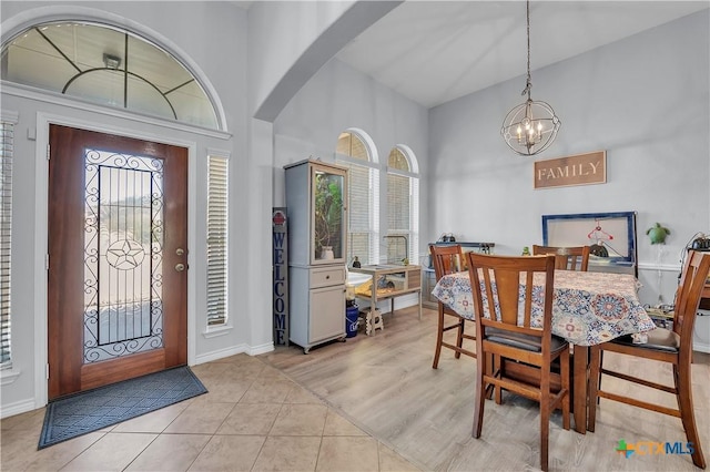 foyer featuring baseboards, light tile patterned floors, a high ceiling, an inviting chandelier, and arched walkways