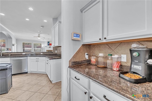 kitchen featuring stainless steel dishwasher, backsplash, dark stone counters, arched walkways, and light tile patterned floors