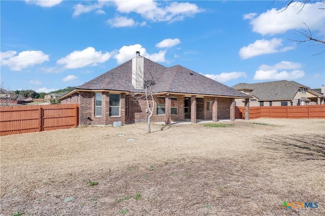 back of house featuring a patio, a fenced backyard, brick siding, and a chimney