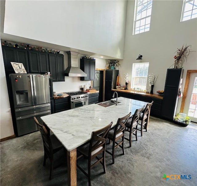 kitchen with wall chimney range hood, sink, a breakfast bar area, stainless steel appliances, and light stone countertops