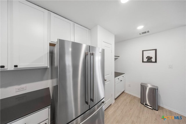 kitchen with visible vents, high end fridge, white cabinetry, baseboards, and light wood-style floors