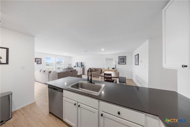 kitchen with a sink, dark countertops, white cabinets, light wood-type flooring, and dishwasher