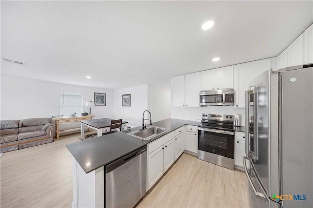 kitchen featuring light wood finished floors, a peninsula, a sink, stainless steel appliances, and visible vents