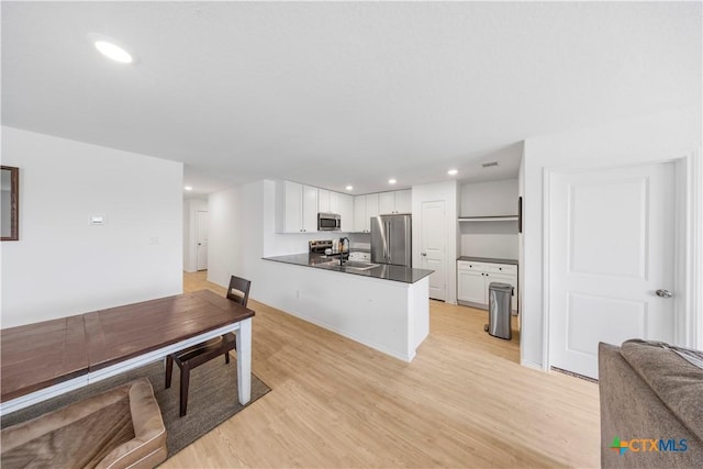 kitchen with stainless steel appliances, open floor plan, white cabinets, dark countertops, and light wood-style floors