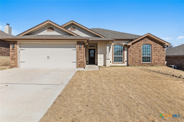 ranch-style home with concrete driveway, a garage, brick siding, and roof with shingles