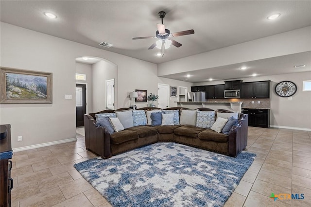 living area featuring light tile patterned floors, a ceiling fan, arched walkways, and baseboards