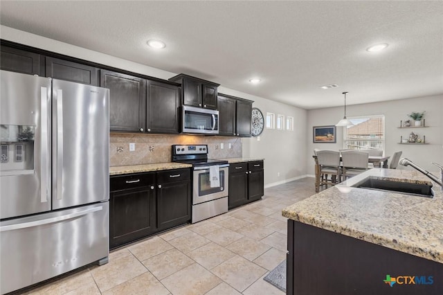 kitchen featuring light stone counters, light tile patterned floors, a sink, stainless steel appliances, and tasteful backsplash